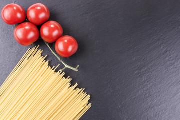 Yellow long raw spaghetti and cherry tomatoes on black slate plate