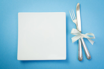 Silver fork and knife with white ribbon and plate on blue background