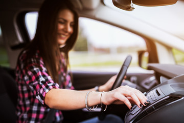 Young cheerful beautiful girl is adjusting a volume of her stereo in the car she is driving.