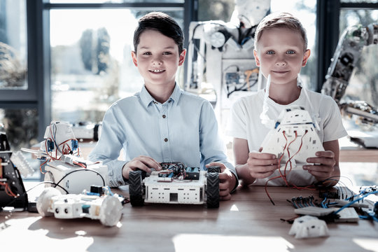 Innovative generation. Waist up shot of smart kids looking into the camera with cheerful smiles on their faces while posing with their self automated robots in hands.