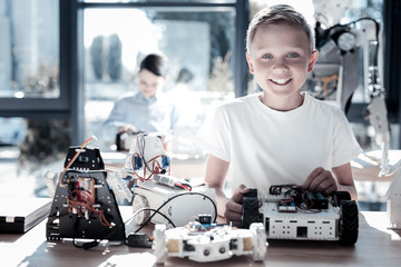 Designing my dream. Waist up shot of an excited schoolboy looking into the camera with his eyes full of happiness while standing at a table and working on his robotic machine in studio.