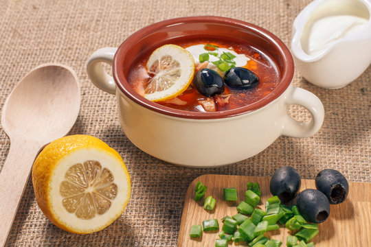 Soup saltwort with meat, potatoes, tomatoes, lemon, black olives and sour cream in ceramic soup bowl
