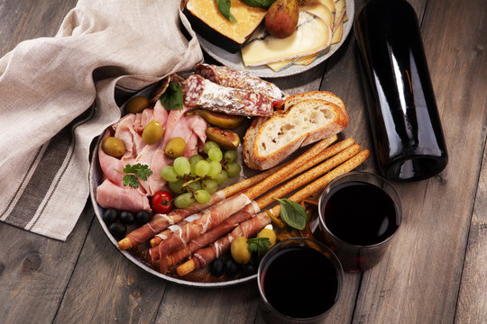 Italian antipasti wine snacks set. Cheese variety, Mediterranean olives, pickles, Prosciutto di Parma, salami and wine in glasses over black grunge background.