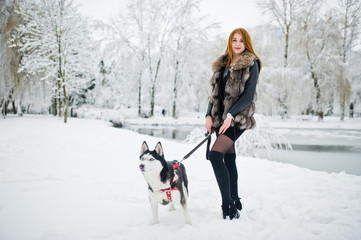 Fototapeta na wymiar Red haired girl walking at park with husky dog on winter day.