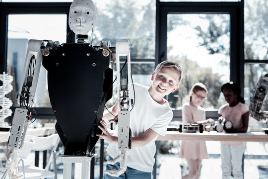 Loving all these innovative technologies. Charming young gentleman looking into the camera and grinning broadly while posing with a human like robot.