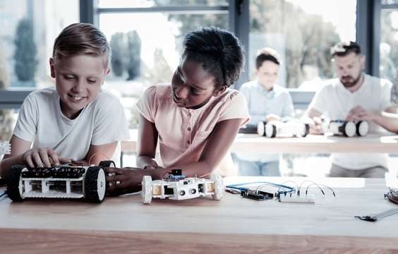Always work as a team. Smart preteen children sitting next to each other and focusing their attention on their new robotic machines while spending their leisure time in a workshop.