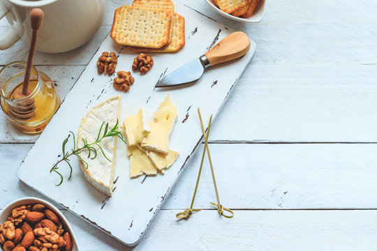 Cheese plate served with crackers, honey and nuts. Camembert on white wood serving board over white texture background. Appetizer theme. Top view with space
