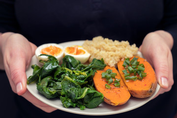 sweet potato with quinoa, boiled egg on plate in womans hands