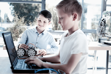 Always working as a team. Selective focus on an adorable boy with a robotic machine smiling while looking at his friend working on a laptop and programming for their new robotic machine.