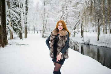 Fototapeta na wymiar Red haired girl in fur coat walking at winter snowy park.
