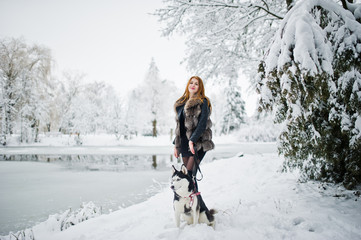 Red haired girl walking at park with husky dog on winter day.