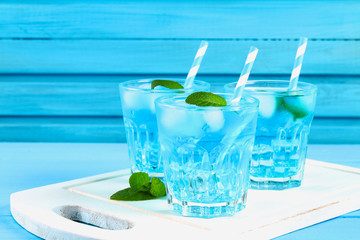 Blue cocktail with ice and mint in glasses on a white wooden board on a blue table.