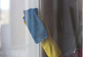 The woman's hand in a yellow glove wipes the window with a dry cloth. Spring Cleaning.