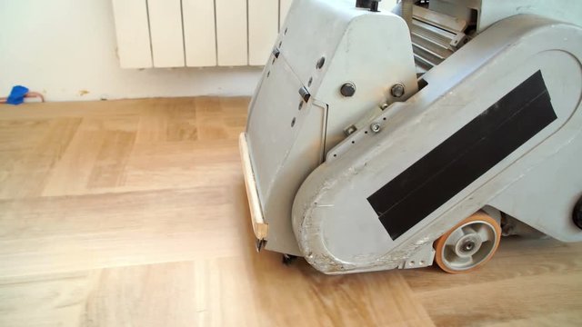 Sanding hardwood floor with the grinding machine. Repair in the apartment. Carpenter doing parquet wood floor polishing maintenance work by grinding machine