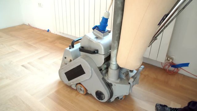 Sanding hardwood floor with the grinding machine. Repair in the apartment. Carpenter doing parquet wood floor polishing maintenance work by grinding machine