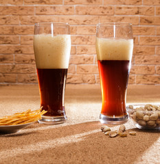 Two glasses of dark beer and a plate of snacks are on the table.