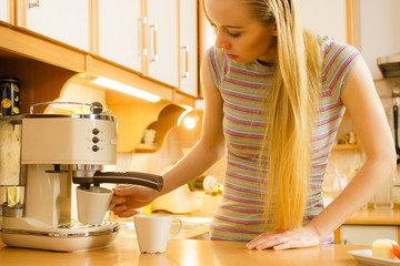 Woman in kitchen making coffee from machine