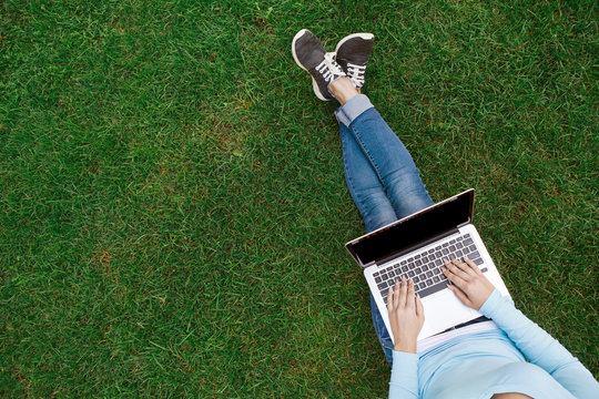 Top view of woman with laptop sitting on the green grass