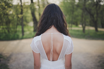 Lovely brooding brunette girl with long hair in white romantic dress in spring forest or park. The...
