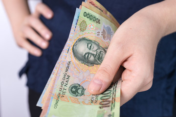 Photo of hand holding folded bundle of blue money in cash of Vietnamese dong. Giving bribe or graft, paying bills or getting salary. Payment day!