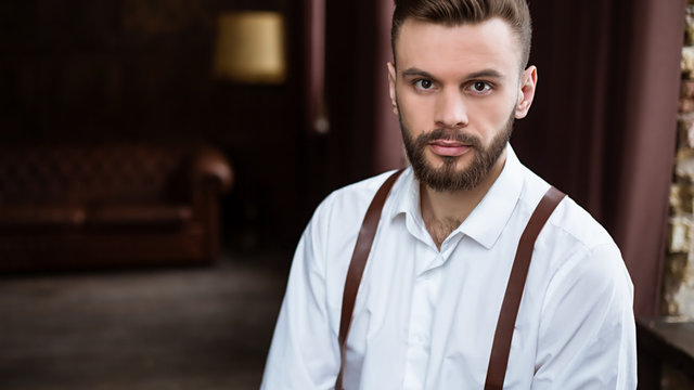 Fashion stylish confident portrair of handsome bearded guy on the big window looking away