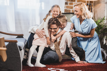 cheerful retro styled family hugging while playing dominoes at home