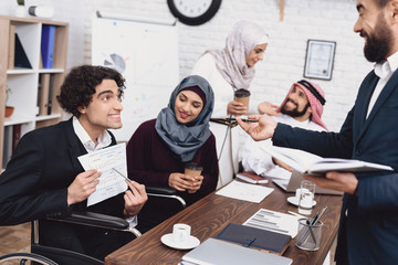 Disabled arab man in wheelchair working in office. Man is sharing notes with coworkers.