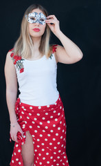 closeup of blonde girl with long hair, with red lips, with white tank top with red floral pattern, with carnival mask Fashion Woman. Uniform black background