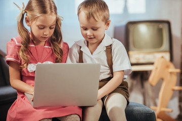 cute little children in 1950s style clothes using laptop together at home