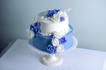 Beautiful two tiered white and blue wedding cake decorated with flowers sugar roses. Concept of elegant holiday desserts