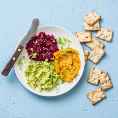 Avocado, beets, turmeric, chickpea hummus and seed crackers on a blue background, top view. Delicious appetizer, tapas, snack