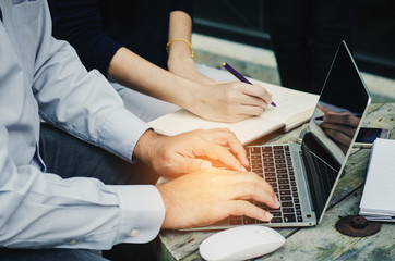 attractive business man working typing on laptop and business woman writing notebook on wood table with calendar and smartphone at outdoor.
