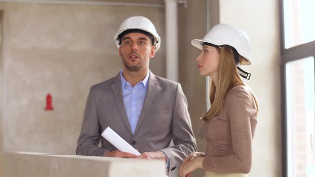 architecture, construction business and people concept - architects with blueprint and helmets at office pointing at something