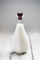 Glass bottle with homemade coconut milk on wooden background. Minimal style