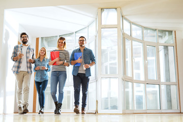 A group of young positive business people walking down the bright hallway for a break.