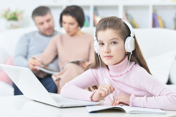 Happy girl sitting at table with laptop with her parents on bac