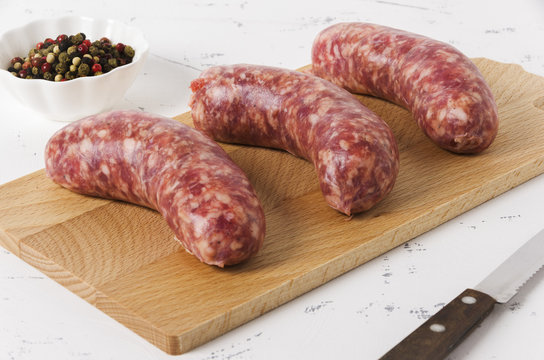 Three sausages on the chopping board on white background and peppercorn