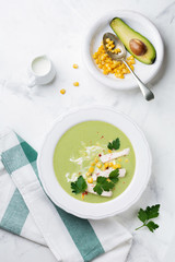 Homemade green soup puree from broccoli, avocado, chicken and corn with cream in rustic ceramic plate on white concrete background. Selective focus. Top view.