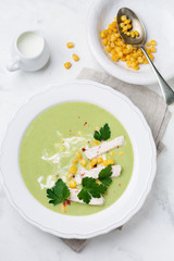Homemade green soup puree from broccoli, avocado, chicken and corn with cream in rustic ceramic plate on white concrete background. Selective focus. Top view.