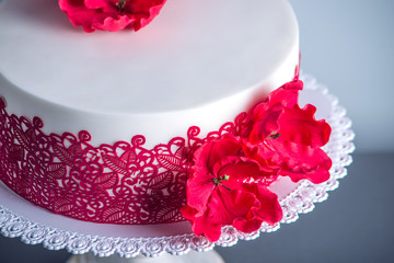 White wedding cake decorated with flowers sugar poppies and red pattern ornament. Concept of elegant holiday desserts