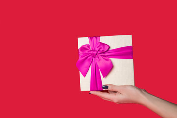 white gift box with a purple bow in his hand on a red background.