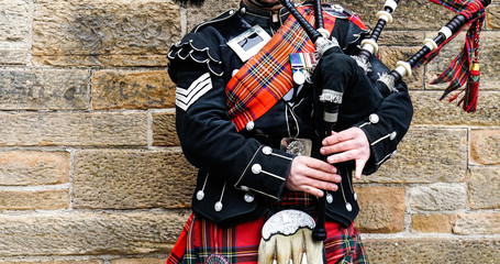 EDINBURGH, SCOTLAND, 24 March 2018 , Scottish bagpiper dressed in traditional red and black tartan dress stand before stone wall. Edinburgh, the most popular tourist city destination in Scotland.