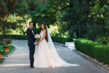 Happy couple hugging and hanging out in the park. The bride in a black suit with a bow tie and a bride in a beautiful white wedding dress with a bouquet of flowers in her hands. Beautiful woman with