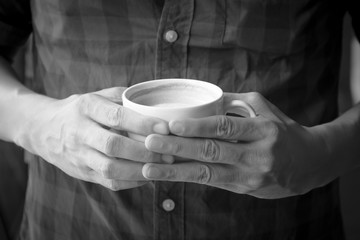 Fototapeta na wymiar Man holding cup of coffee in his hands; picture color by black and white