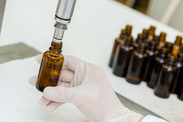 Close up of female lab worker hand with gloves filling the bottle with syrup