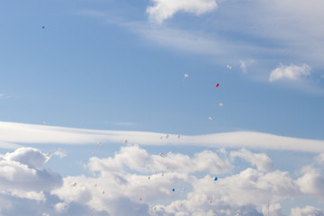 Colorful balloons fly in the blue spring sky with white clouds