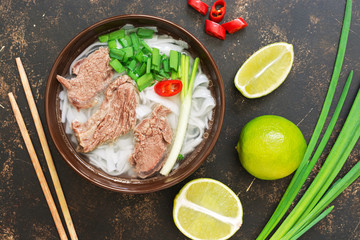 Traditional Vietnamese pho soup on a dark rustic background, lime, green onions, chili. View from above.