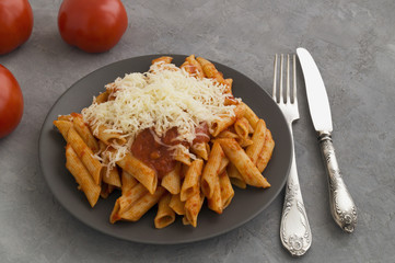 Penne pasta with tomato sauce on grey background.