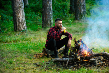 Handsome macho with beer sitting near bonfire,