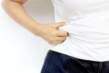 Close up fat Asian woman stand and hand squeeze her fat at belly on white wall have copy space. Concept overweight should diet to lose weight for health.